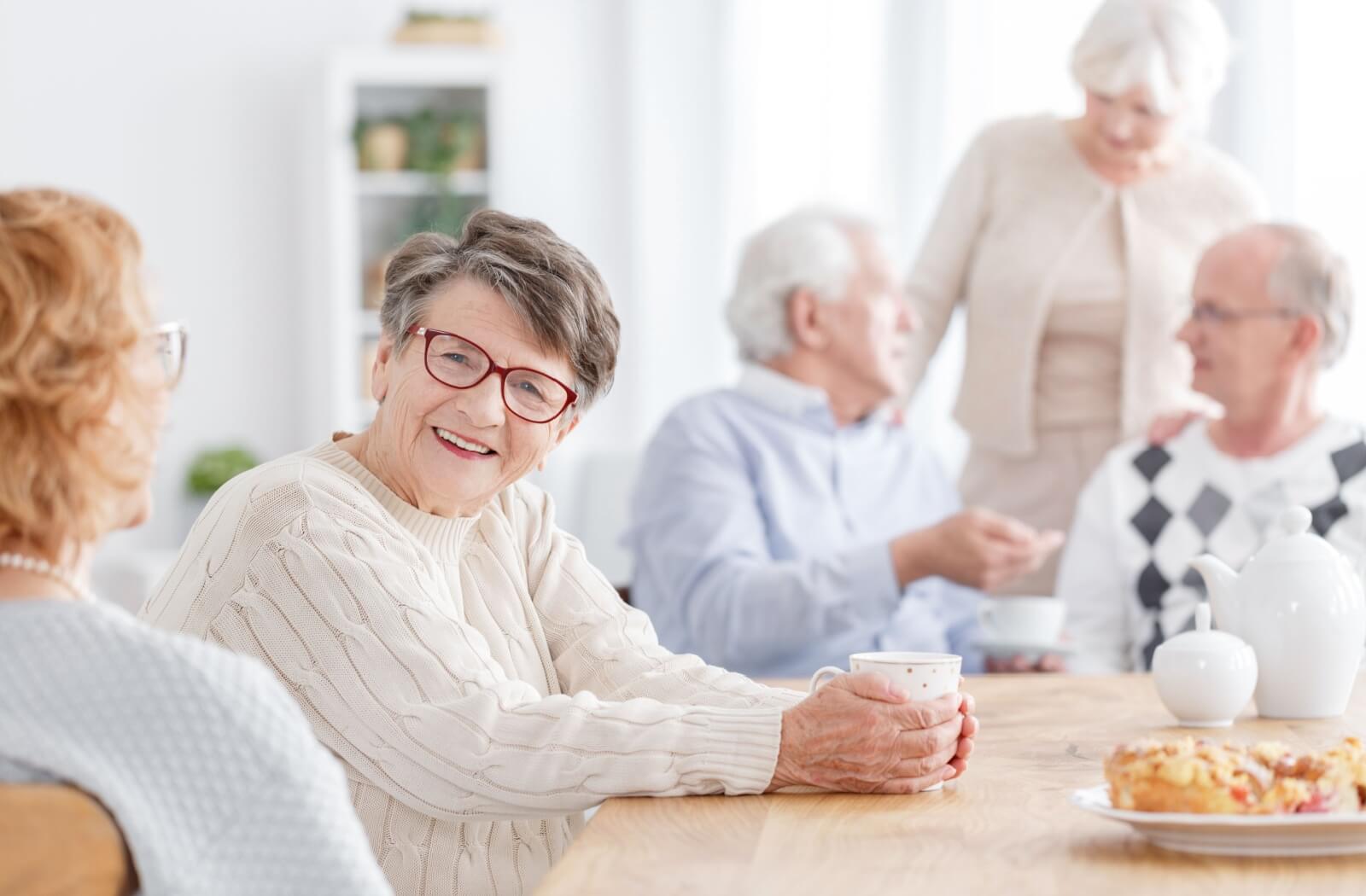 A senior holds a cup of coffee while talking with other memory care residents over breakfast