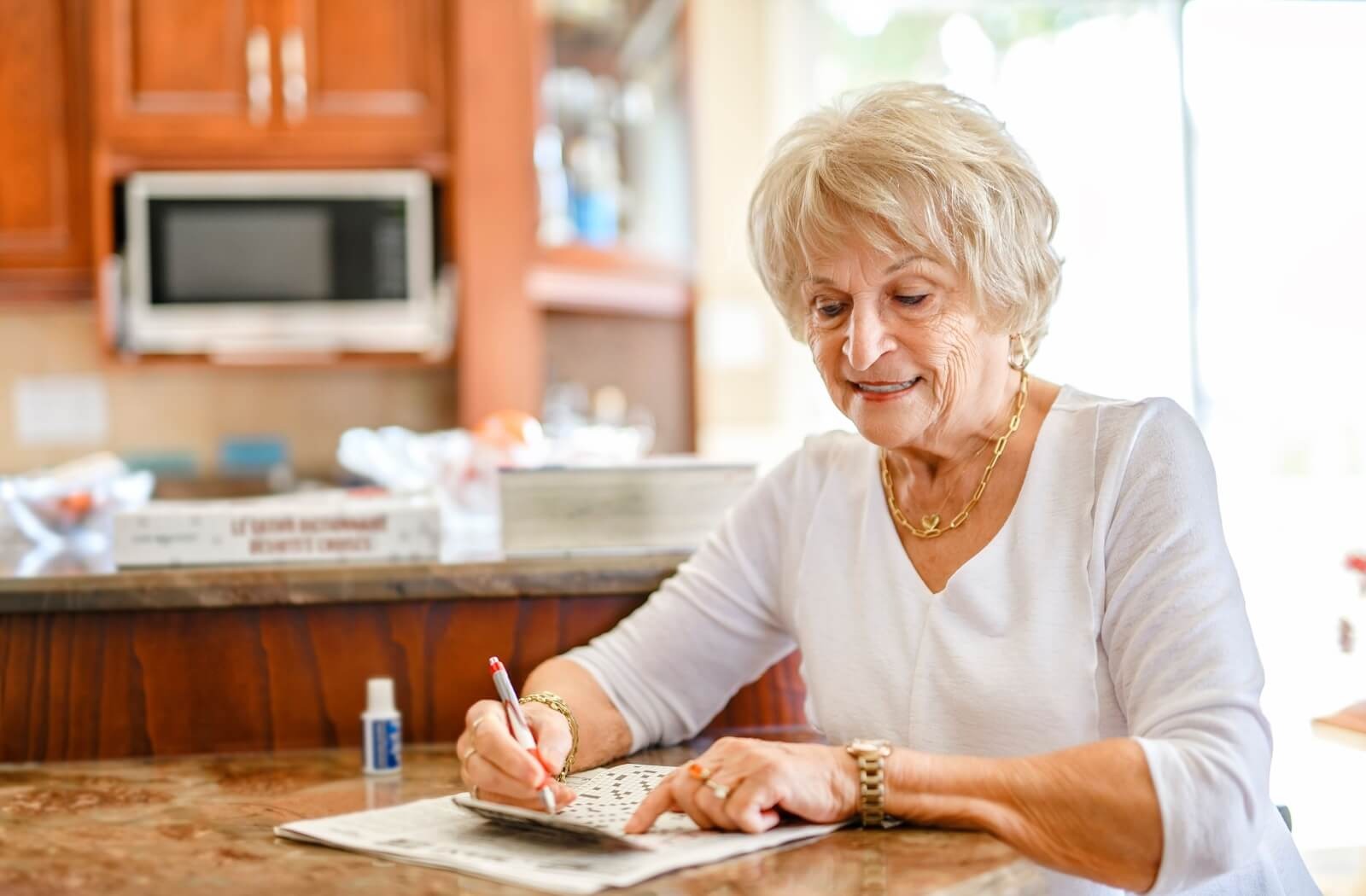An older adult smiles while doing a crossword puzzle in their kitchen in memory care
